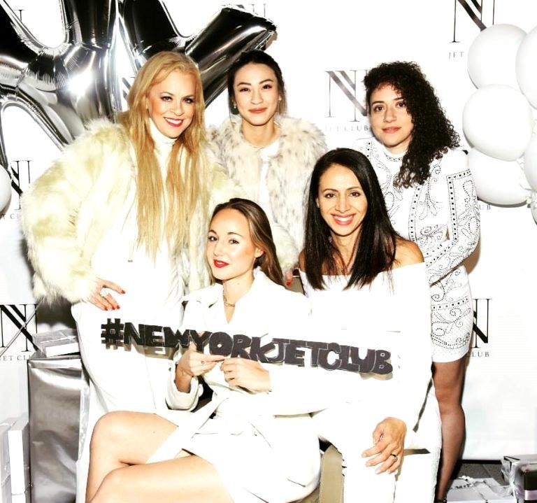 Five women in white holding '#NEWYORKJETCLUB' sign