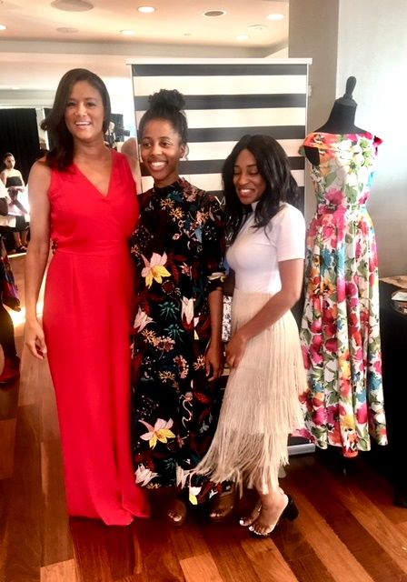 Three women posing beside floral dress mannequin