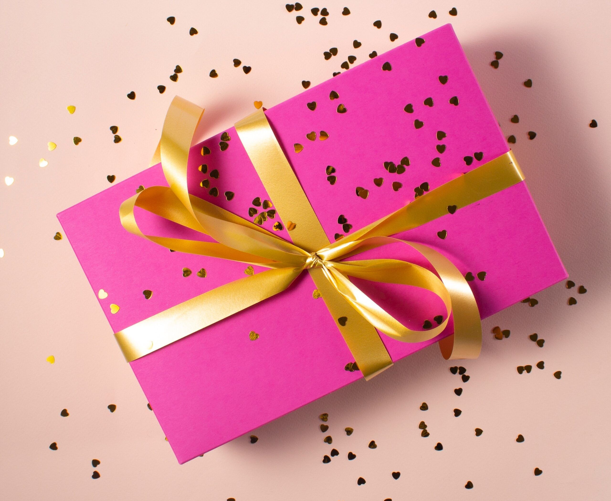 Pink gift box with gold ribbon and confetti