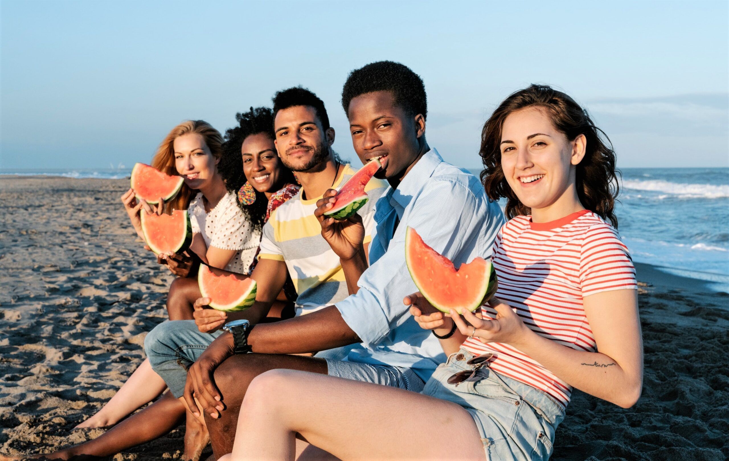 Smiling friends eating watermelon on beach