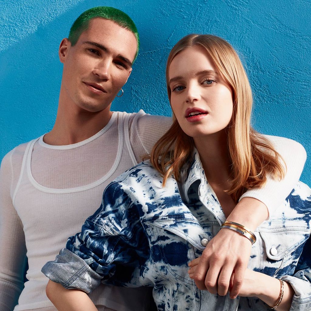 Two fashion models posing against blue wall