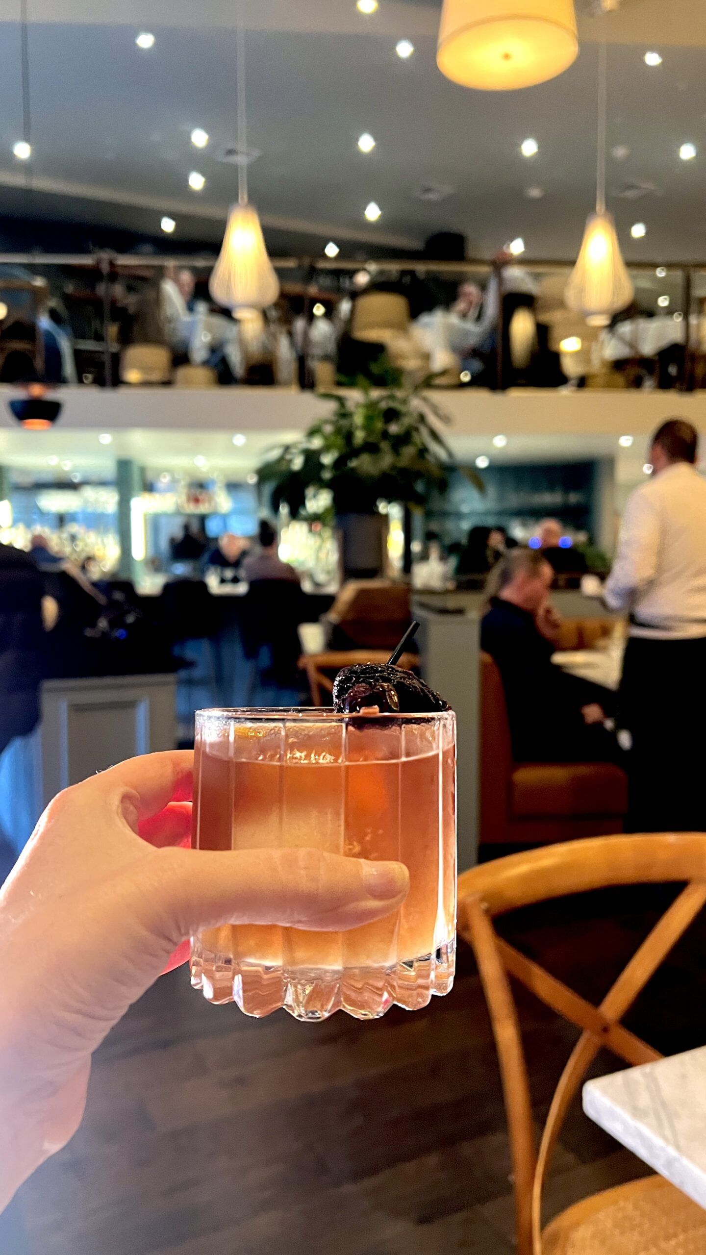 Hand holding cocktail in busy restaurant