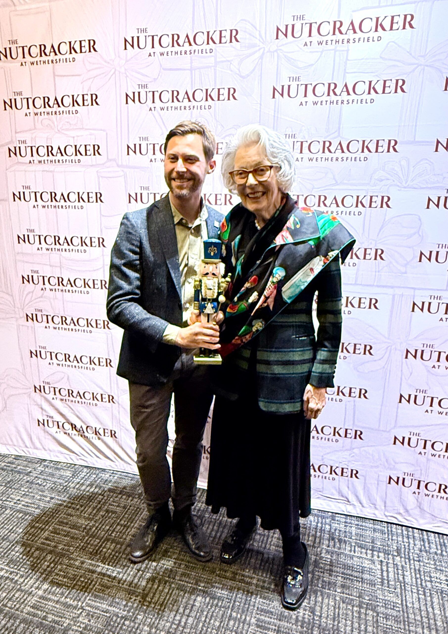 Two people holding nutcracker by event backdrop