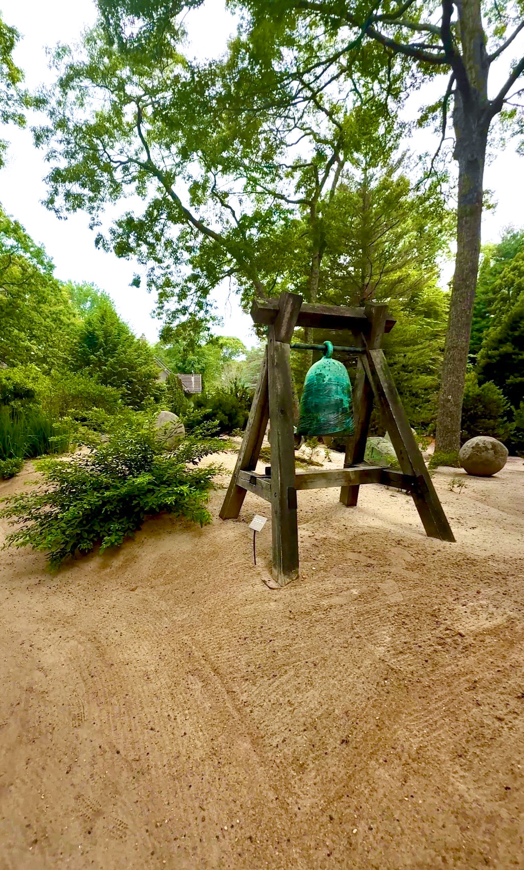 Green bell hanging from wooden garden frame