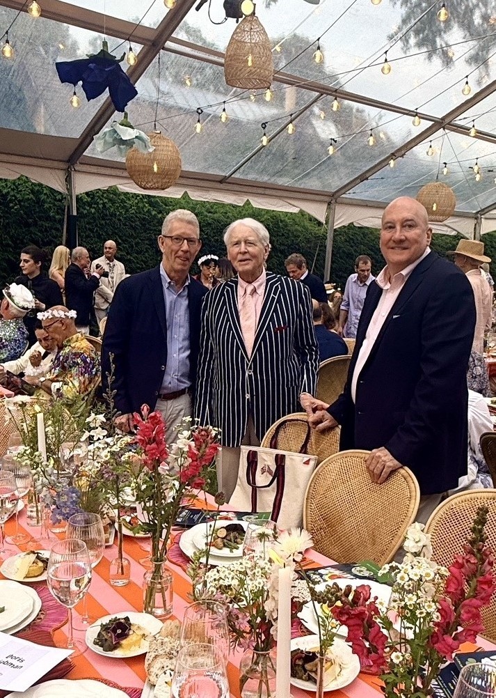 Three men posing by decorated outdoor banquet table
