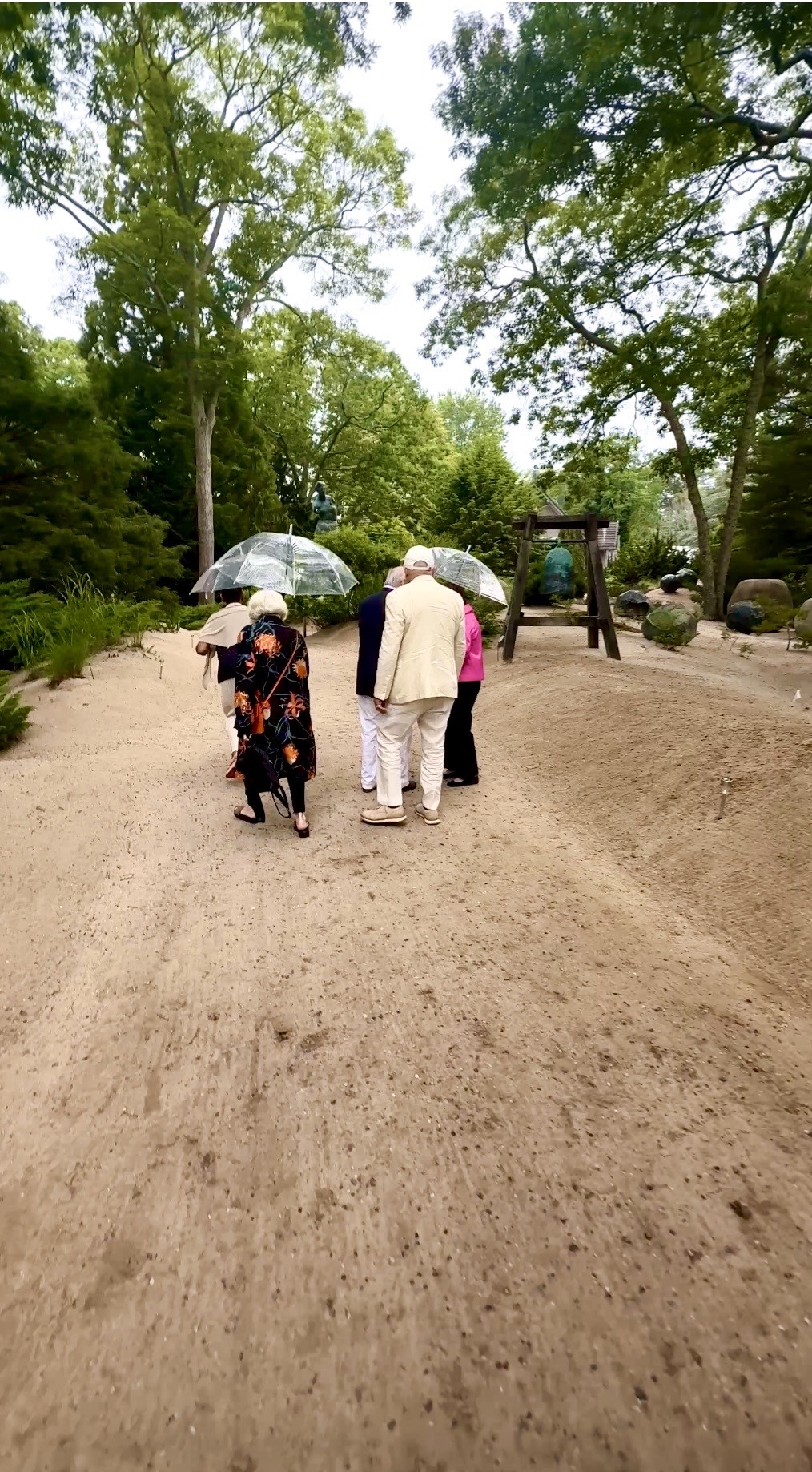 Seniors walking on sandy garden path with umbrellas