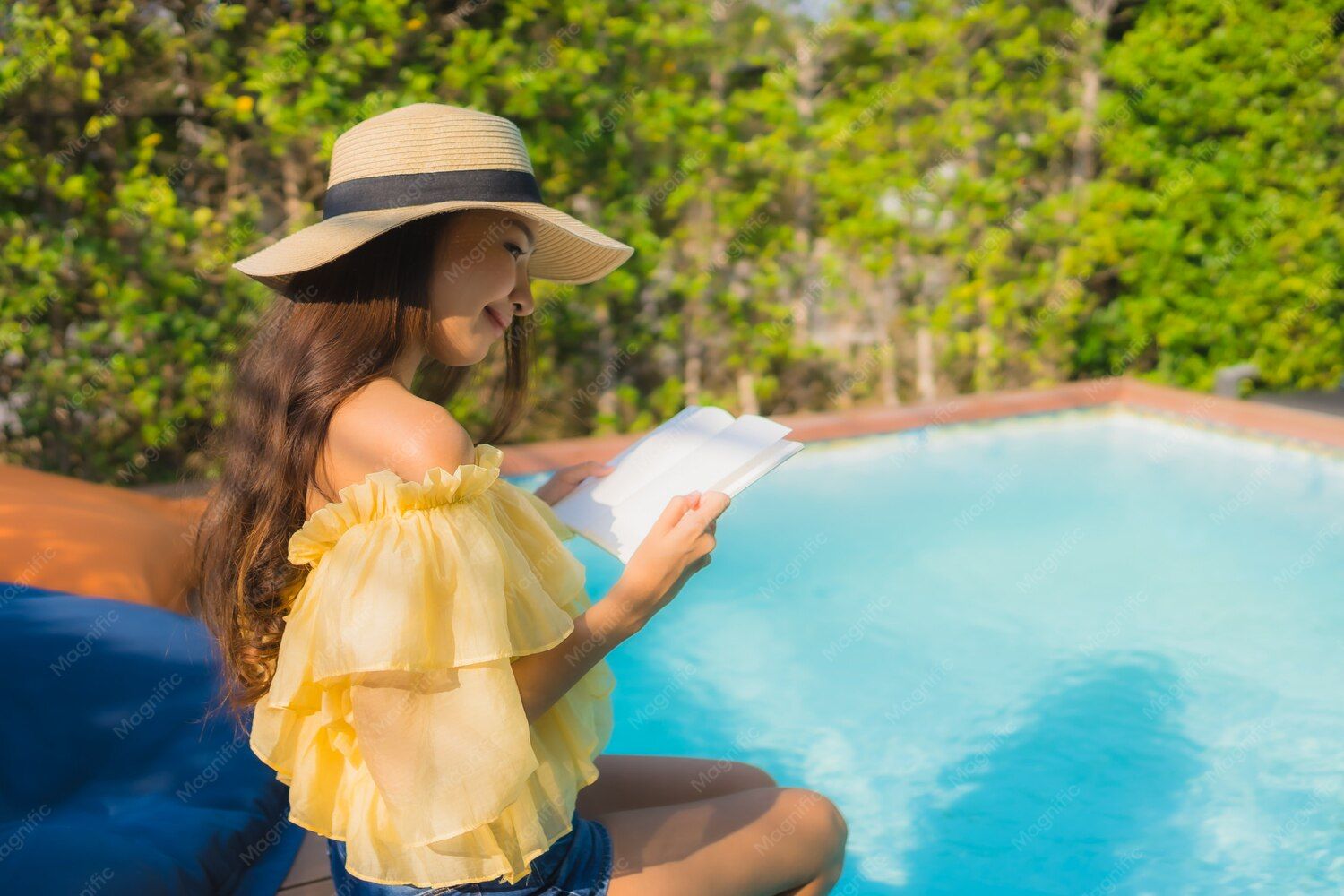 Woman reading book beside pool in sunhat